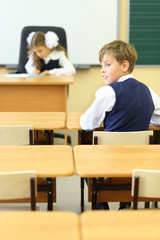 Girl sits at teacher table and writes and boy sits at desk