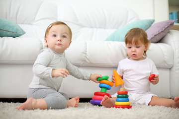 Obraz na płótnie Canvas Two little kids sit on carpet and play with pyramids near sofa.