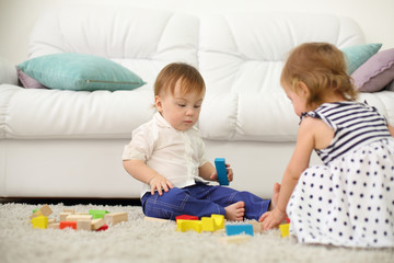 Two barefoot kids sit on carpet and play with wooden cubes