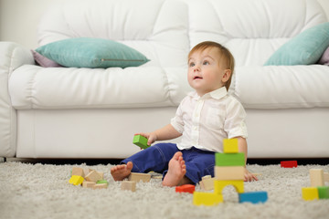 Barefoot baby sits on carpet with wooden cubes and looks up