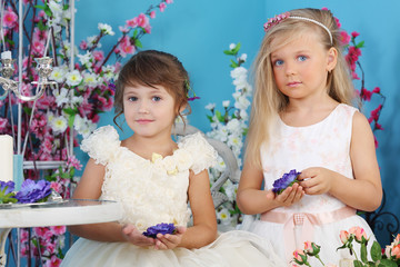Two pretty little girls in white dresses hold blue flowers