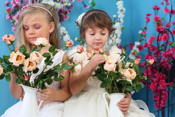 Two little girls in white dresses looks at bouquets of roses