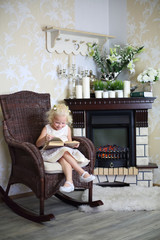 Obraz premium Little smiling girl sits in wicker rocking chair with book