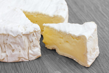 Slice of white cheese cut out of a big round on a wood surface.