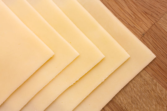 Sliced yellow sandwich cheese arranged on wood
