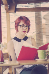 Fototapeta na wymiar Cute hipster teenage girl reading a book and enjoying coffee
