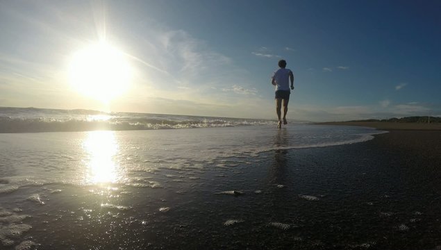 Man running on the beach at sunset. Sunny summer day