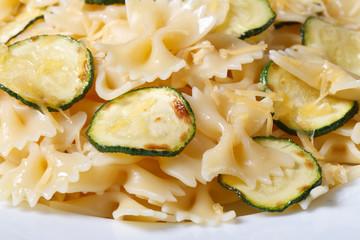 Farfalle pasta with zucchini and cheese on a white plate macro