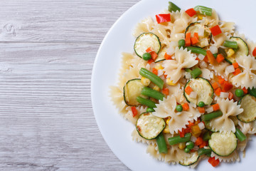 Tasty salad of farfalle pasta with vegetables closeup top view
