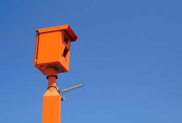  Traffic speed camera of orange color under blue sky .  Photographed in Israel. 