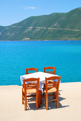 Dining table with chairs in a greek taverna with blue sea and gr