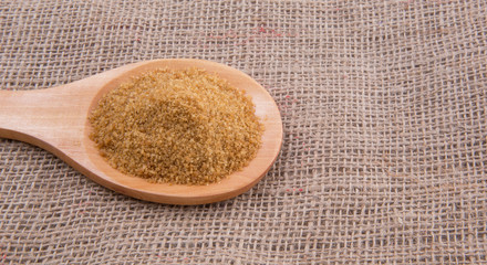 Brown sugar in wooden spoon on gunny sack background