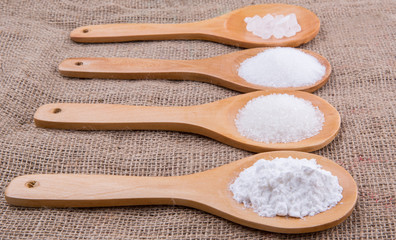 Various type of white sugar in wooden spoon on gunny sack