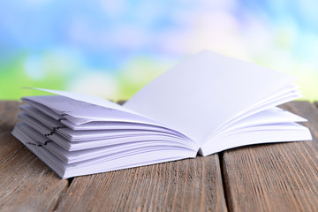 Open white book on wooden table on bright background