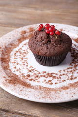 Chocolate muffin with red currant on plate on wooden background