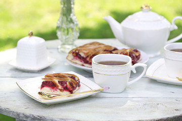 Coffee table with teacups and tasty pie in garden