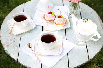 Coffee table with teacups and tasty cakes in garden