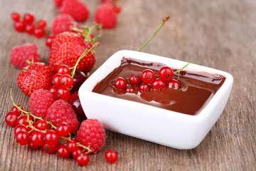 Ripe sweet berries and liquid chocolate on wooden table