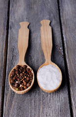 Salt and pepper in spoon on wooden table close-up