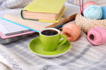 Cup of coffee and yarn for knitting on plaid with books