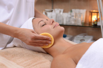 Relaxed female getting face cleaned with facial sponges by professional cosmetologist at the spa