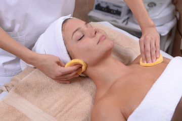 Relaxed female getting face cleaned with facial sponges by professional cosmetologist in spa treatment