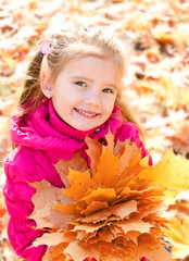 Fototapeta premium Autumn portrait of cute smiling little girl with maple leaves