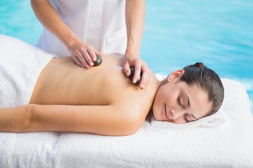 Fototapeta na wymiar Happy brunette getting a hot stone massage poolside
