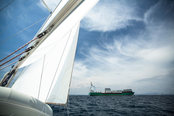 Obraz premium Cargo ship on the high seas, in the foreground sail yacht.