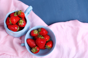 Ripe sweet strawberries in mugs  on color wooden background