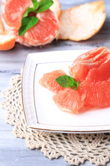 Ripe peeled grapefruits on plate, on color wooden background