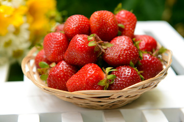 Ripe sweet strawberries in wicker basket on table in garden