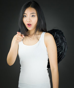 Shocked Asian young woman dressed up as an angel pointing