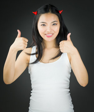 Asian young woman in devil horns showing thumb up sign with both