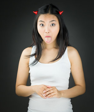 Asian young woman in devil horns sticking out her tongue