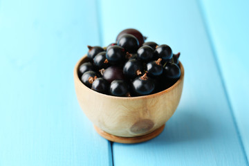 Ripe blackcurrants in bowl on wooden background.