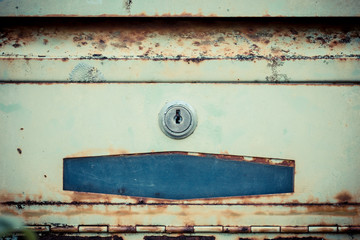 Rusty mailbox hangs off a metal fence.