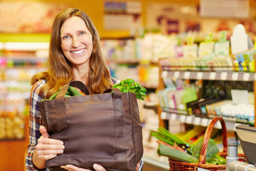 Lächelnde Frau trägt Einkaufstasche mit Gemüse - obrazy, fototapety, plakaty