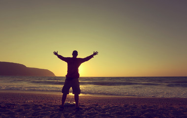 Fototapeta premium young man hands up on a beach at sunset