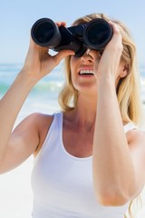 Blonde looking through binoculars on the beach