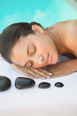 Obraz na płótnie Canvas Smiling brunette lying on towel having a hot stone massage