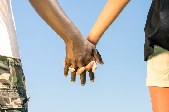 Multiracial couple walking hand in hand against a blue sky
