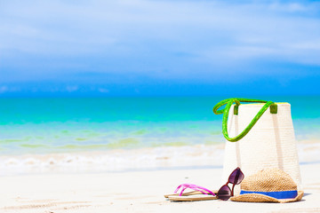 beach bag, sunglasses and flip flops at tropical beach.