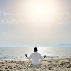 man practicing yoga meditation on the beach