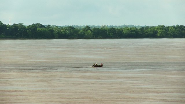 distance view of a small wooden fishing boat crossing river