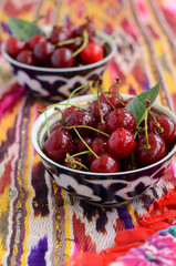 Ripe cherry in oriental bowls on bright ethnic fabric