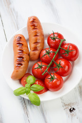 Plate with grilled sausages and a branch of roasted tomatoes