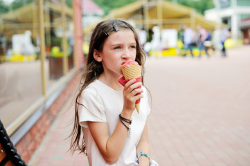 Cute brunette kid girl eating strawberry ice cream in the city