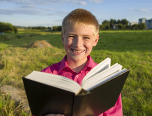 The boy reads the book outdoors