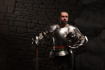Medieval Knight posing with sword in a dark stone background